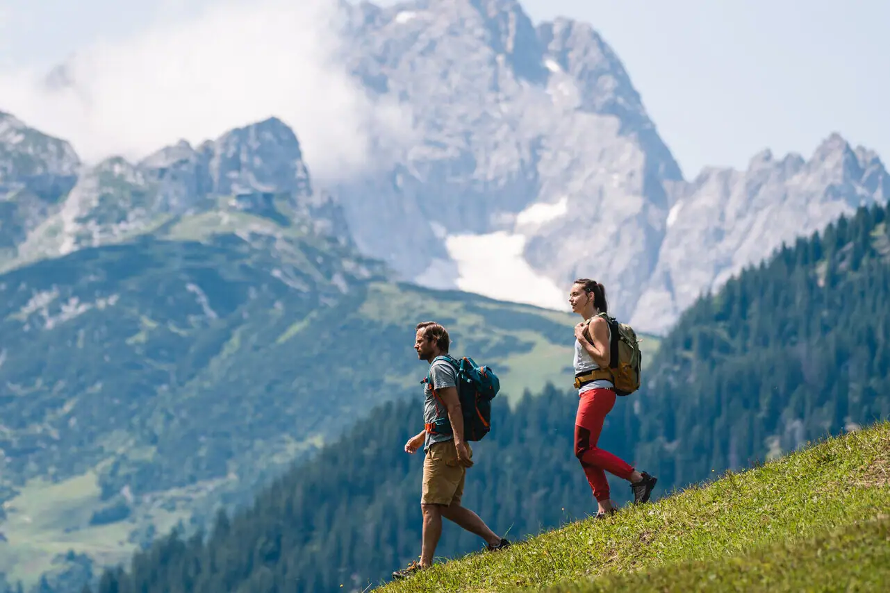 Wandern Garmisch Zwei Personen wandern auf einem Hügel mit Bergen im Hintergrund.