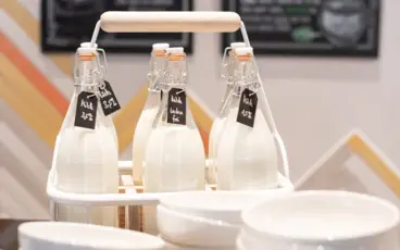 In einer Halterung stehen sechs Glasflaschen mit frischer Milch. Davor stehen kleine Stapel an weißen Schälchen.