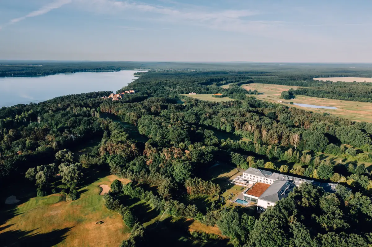 aja Bad Saarow Ein großes Gebäude umgeben von Bäumen und einem Gewässer.