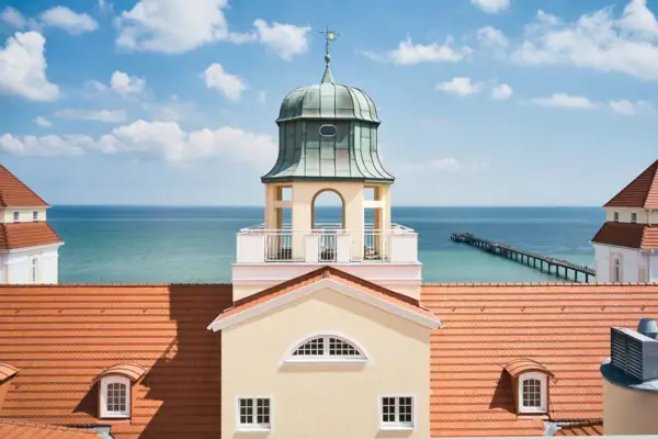 Kurhaus Binz Ein Gebäude mit Turm im Vordergrund und einem Pier im Hintergrund.