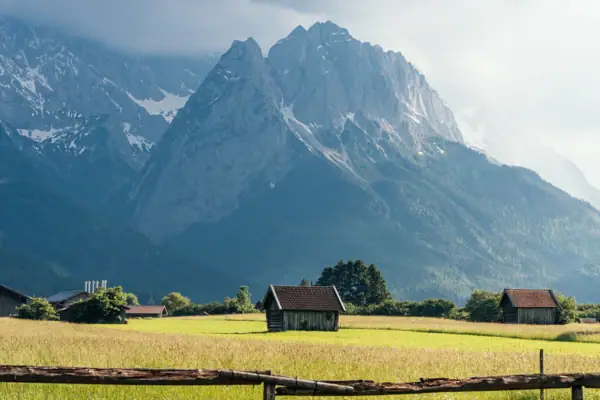 Alpspitzblick & Tegernauweg Ein Holzzaun in einem Feld mit Bergen im Hintergrund.