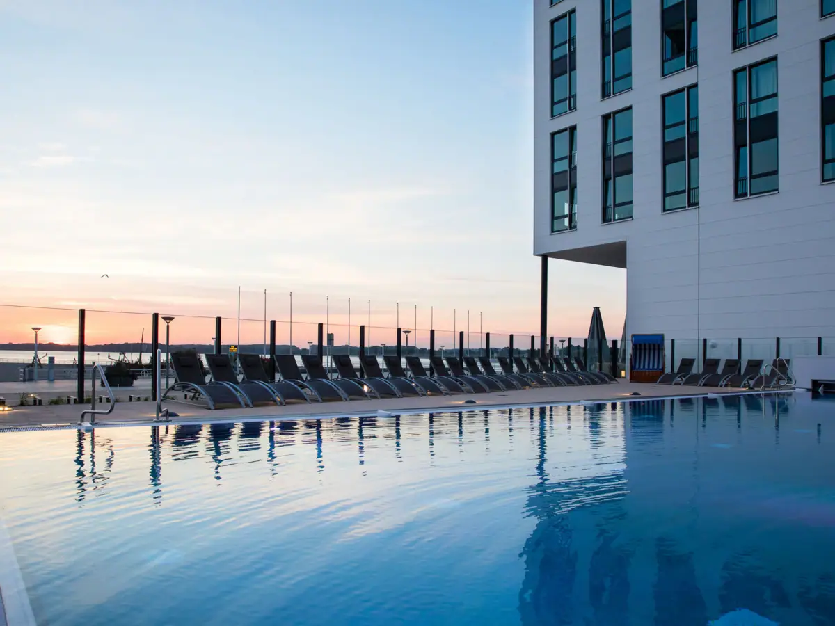 Außenpool aja Travemünde Ein Pool mit Stühlen und einem Gebäude im Hintergrund.