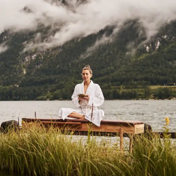 Yoga Eine Frau sitzt auf einer Bank am See.
