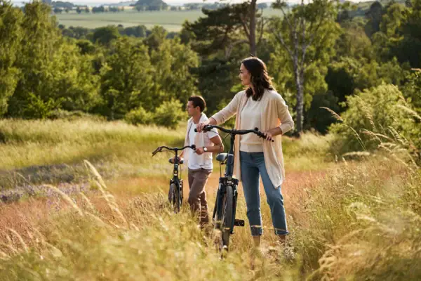 Fahrradtour Rügen Paar mit Fahrrädern steht inmitten einer sommerlichen Wiesenlandschaft auf Rügen; sie genießen den Ausblick über die hügelige Natur und blühende Felder unter freiem Himmel.