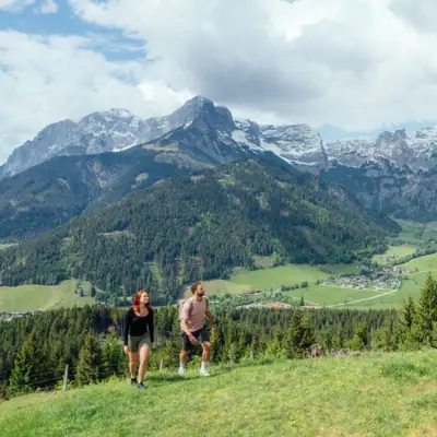 Wandern Ein Mann und eine Frau wandern auf einem Hügel mit Bergen im Hintergrund.