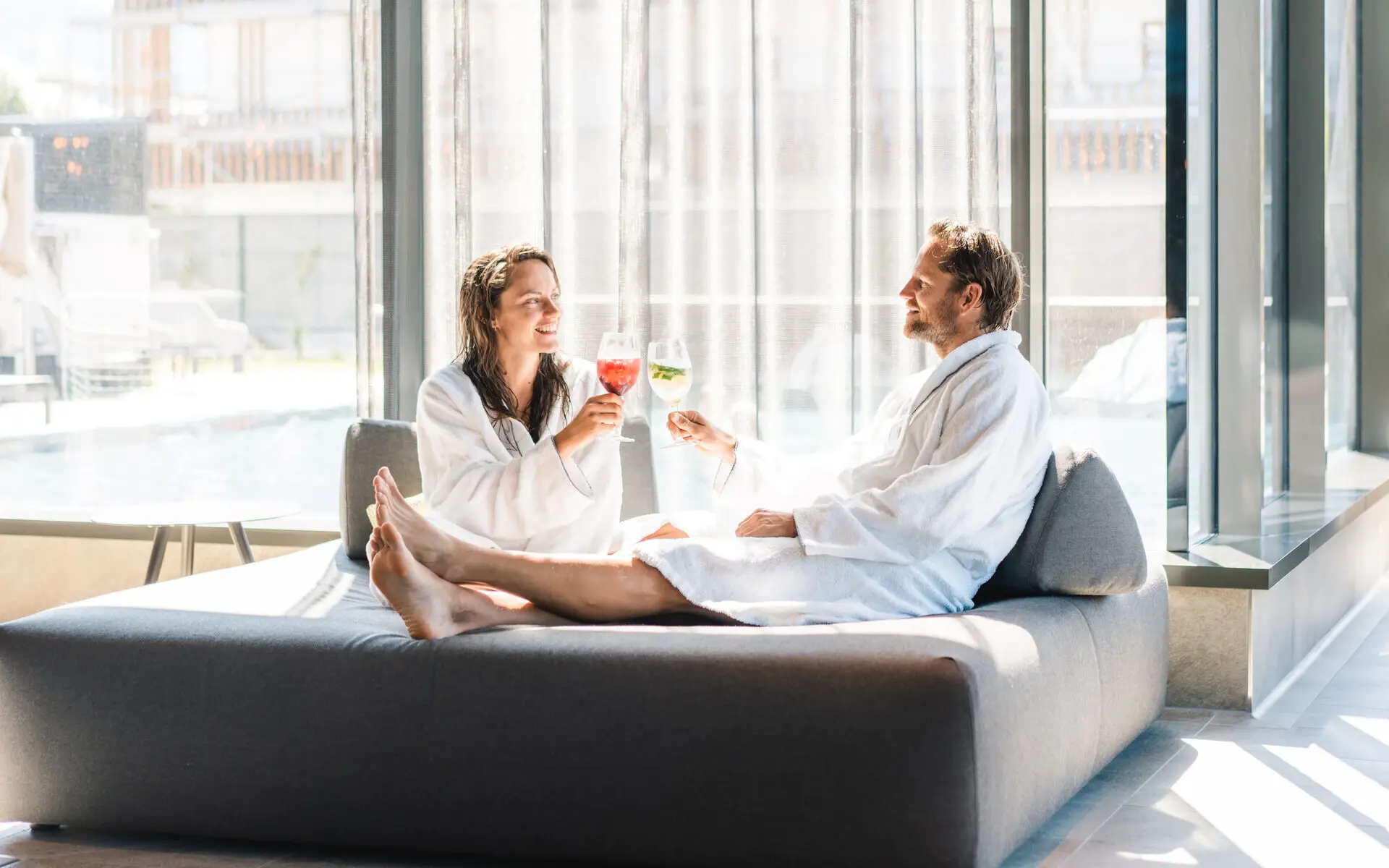 Ruhebereich im SPA aja Garmisch-Partenkirchen Ein Mann und eine Frau stoßen an und entspannen in Bademänteln im Loungebereich des SPA aja Garmisch-Partenkirchen
