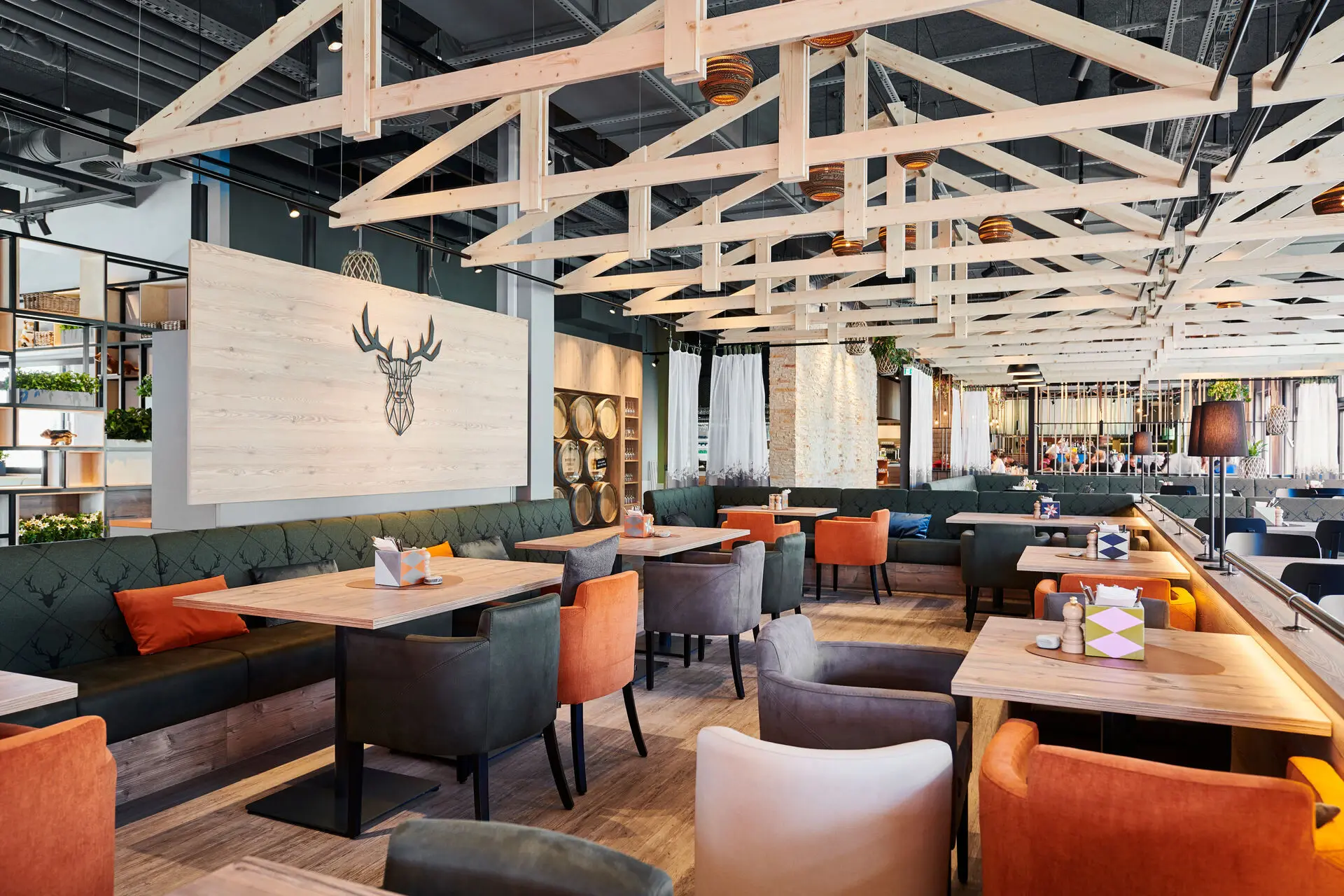 Ein modernes Restaurant mit Holzbalken und hölzernen Trennwänden sowie Sitzmöglichkeiten in orange und dunkelgrau für Gäste.