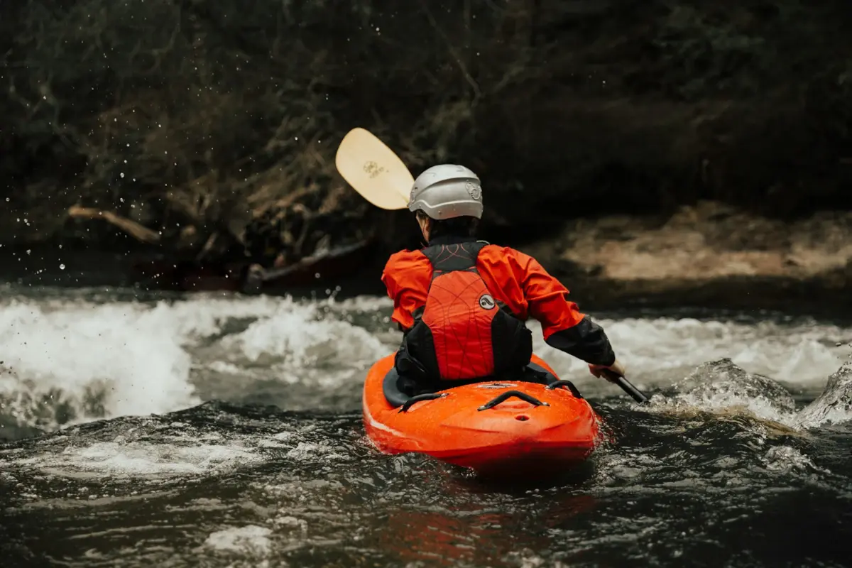 Kajak Eine Person in einem Kajak mit Schwimmweste und Paddel auf einem Fluss.