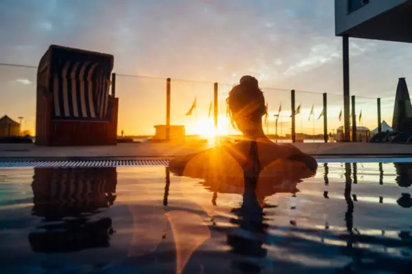 Eine Frau sitzt in einem Pool mit Sonnenuntergang im Hintergrund.