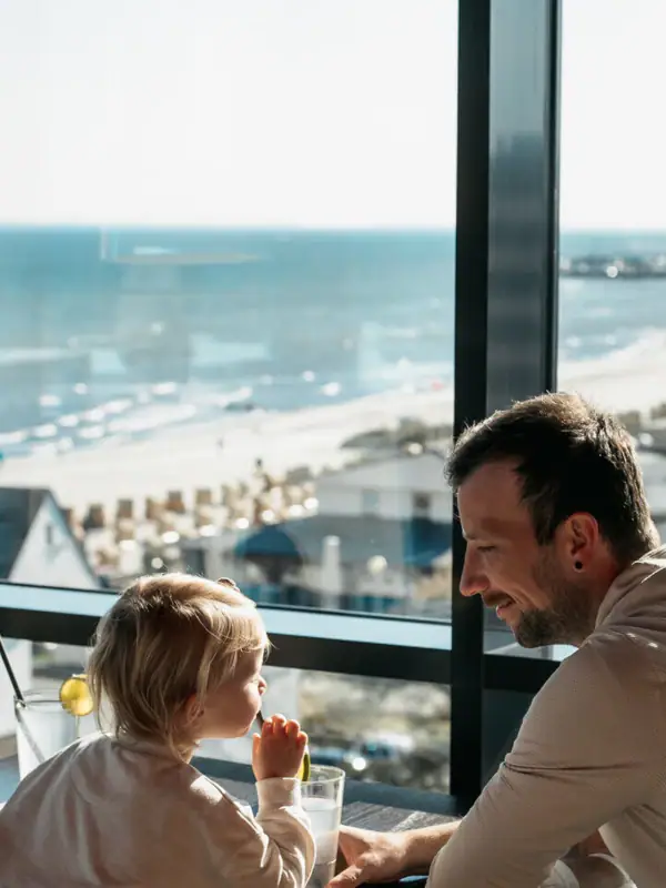 Bar Ein Mann und ein Kind sitzen an einem Tisch und schauen auf einen Strand.
