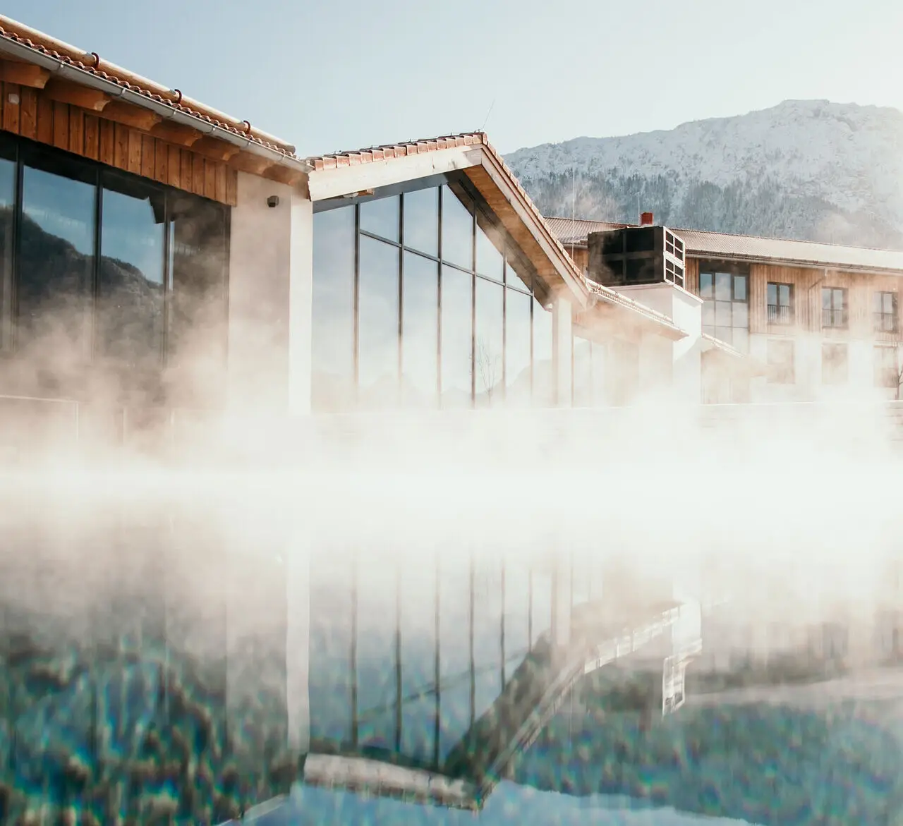 Ein Mann schwimmt in einem warm dampfenden Pool mit Blick auf die schneebedeckte Umgebung.