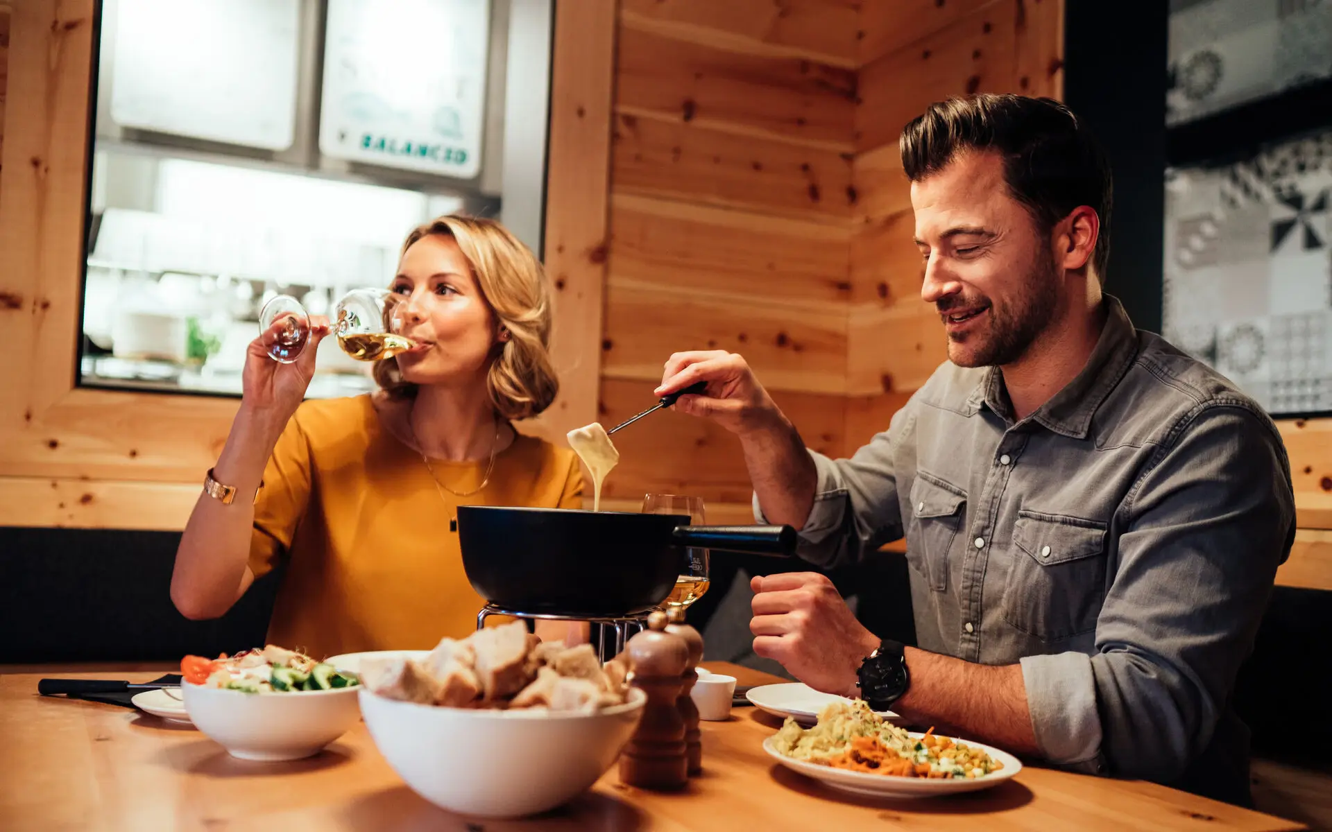 Ein Paar sitz in einem Restaurant mit Holzambiente und genießt Käsefondue.
