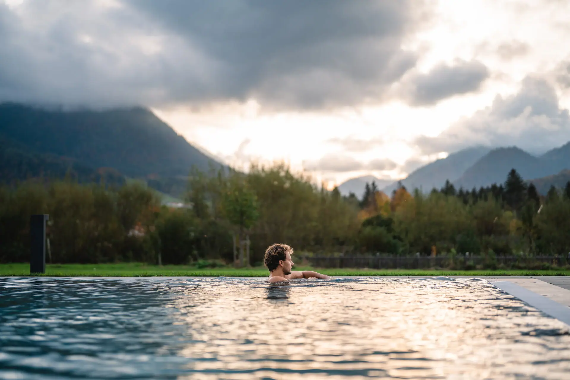 Außenpool aja Ruhpolding Ein Mann im Pool mit Bergen im Hintergrund.