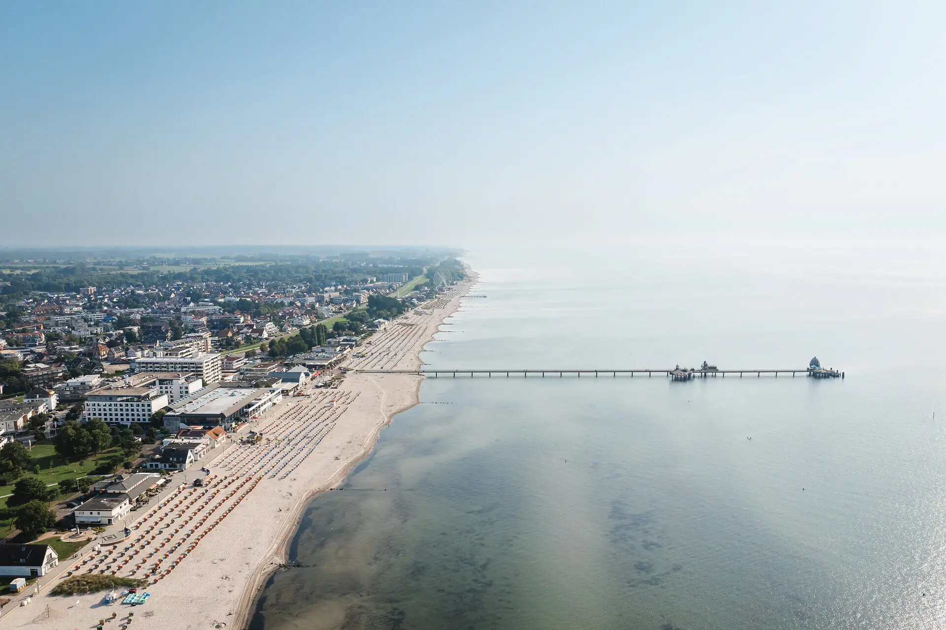 Strand mit einem Pier und Gebäuden im Hintergrund.