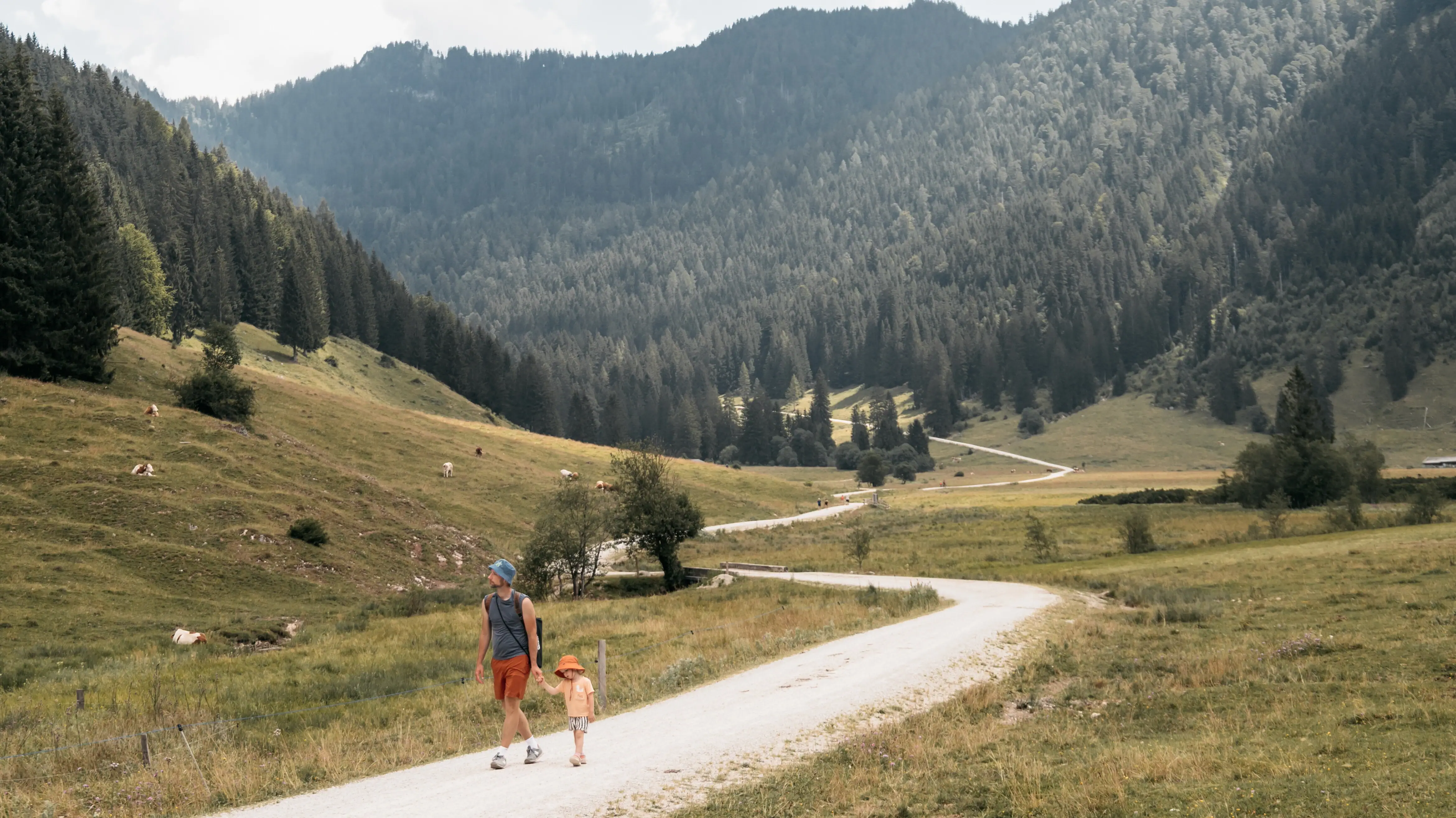Wanderung Eine Frau und ein Kind gehen auf einem Feldweg in einer grasbewachsenen Gegend mit Bäumen.
