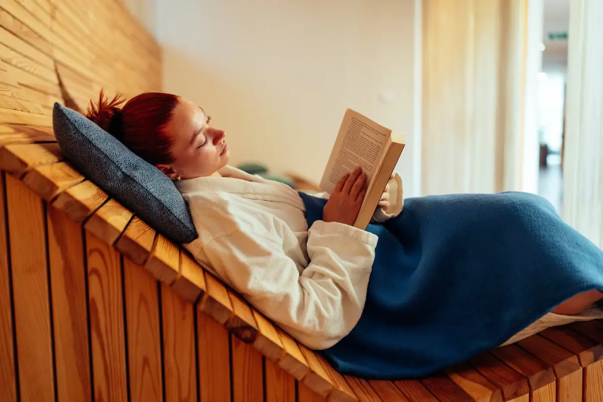 Wellness-Wochenende mit aja Eine Frau liegt auf einer Holzbank und liest ein Buch.