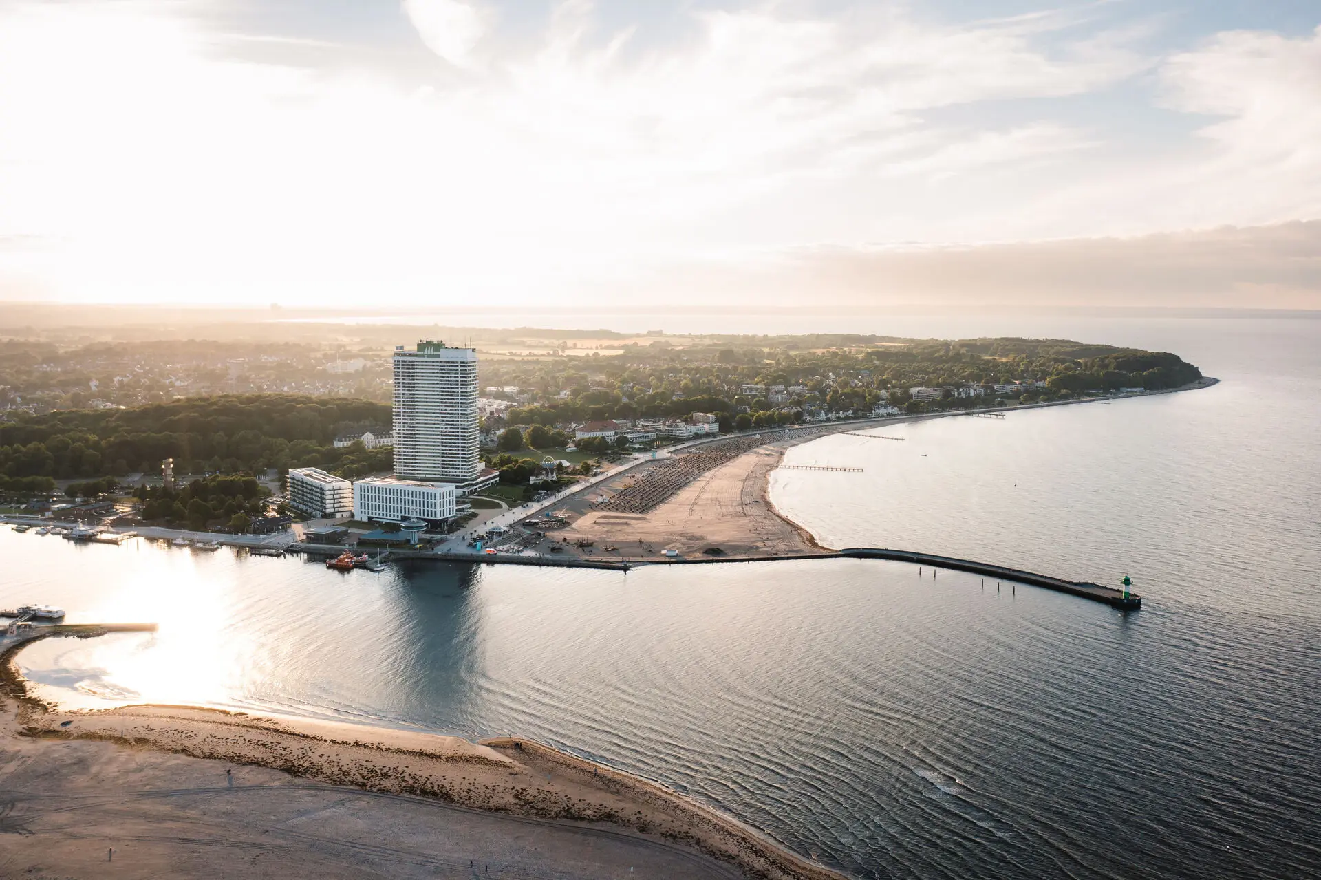 aja Travemünde Strandlandschaft mit Gewässer und einem hohen Gebäude im Hintergrund