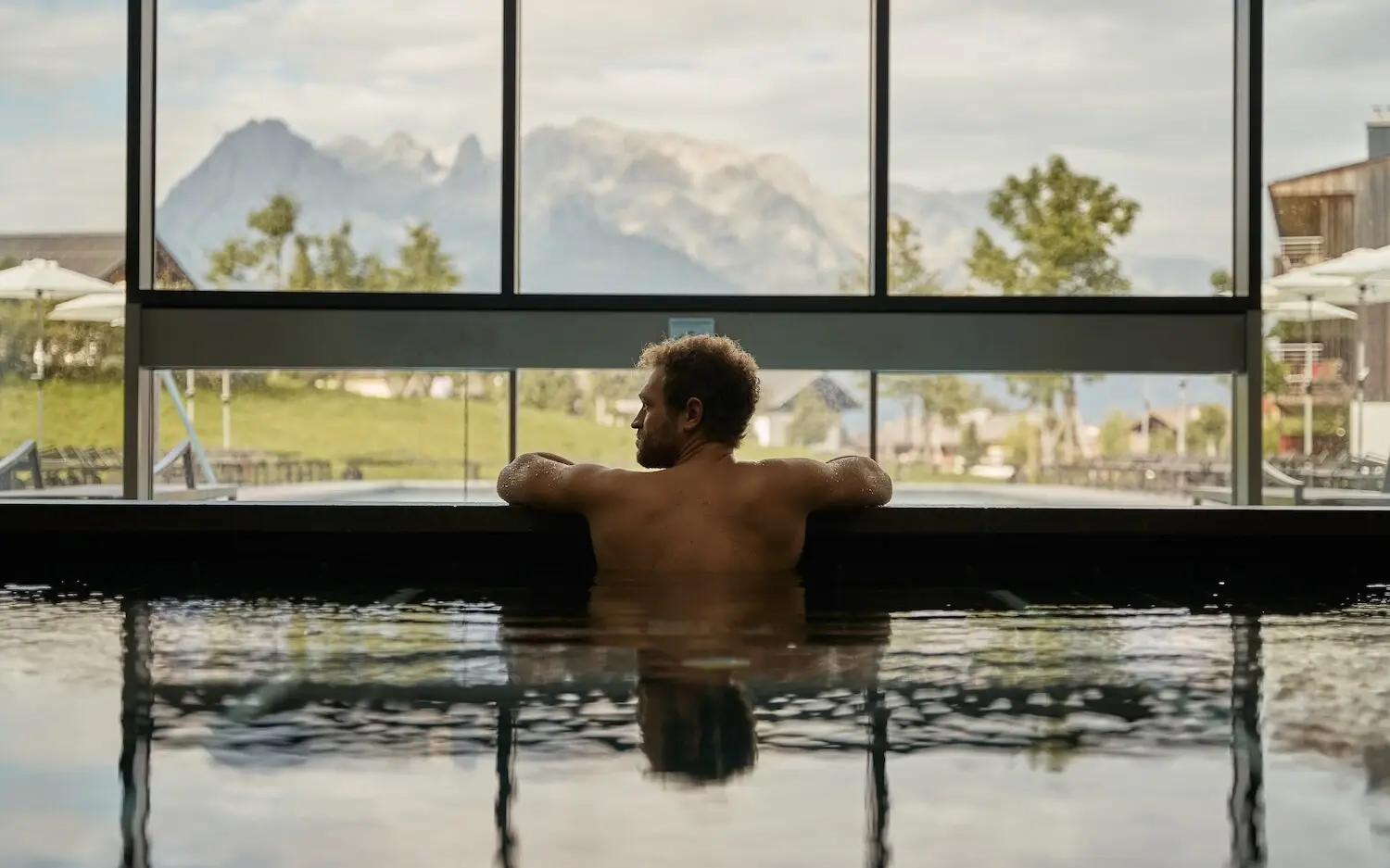 Innenpool aja Werfenweng Mann schwimmt in einem Pool mit Berg- und Baumblick.