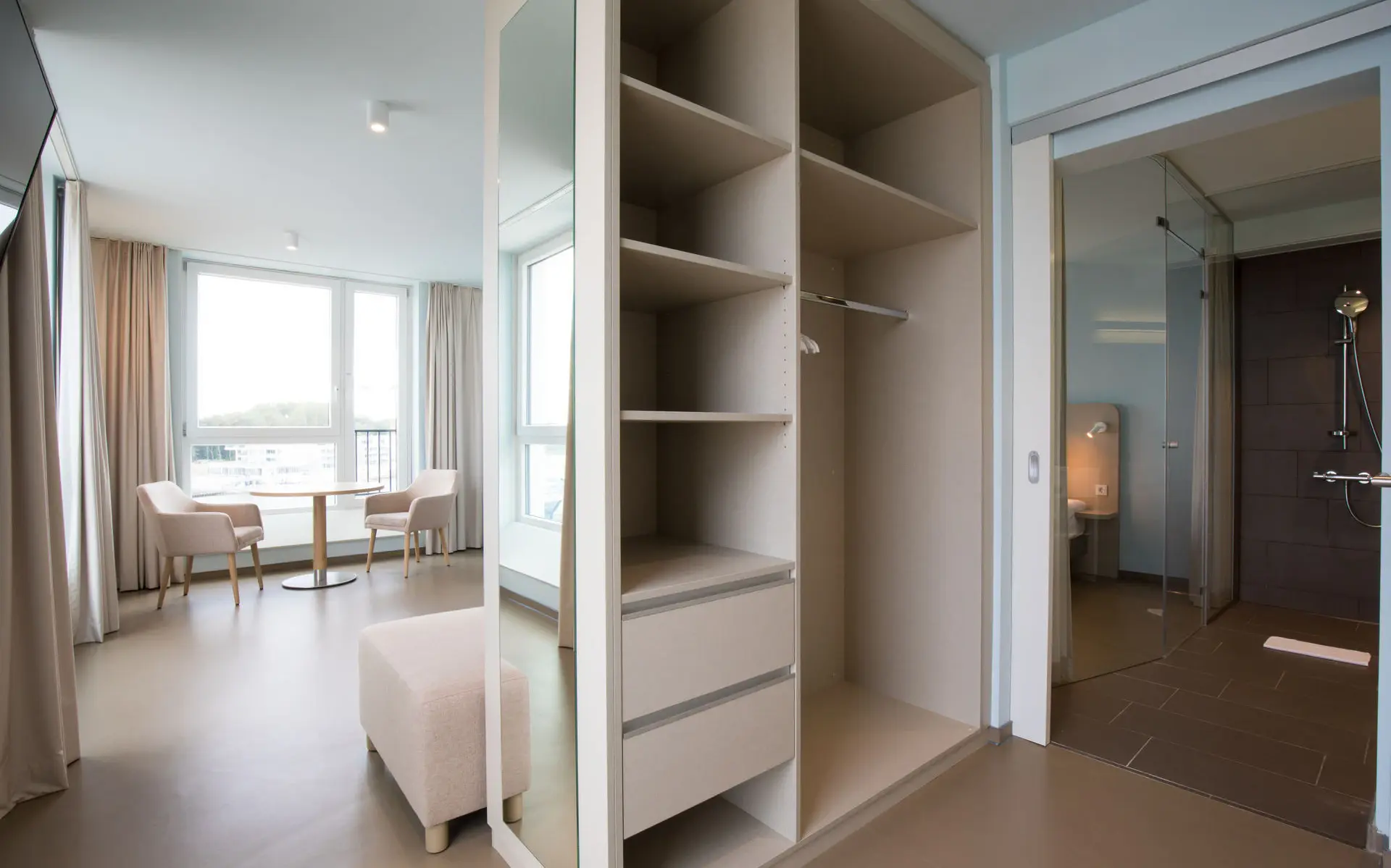 Ein Zimmer mit Schrank, Dusche und im Hintergrund zwei Stühle mit Tisch