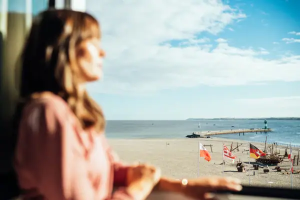 Zimmeraussicht Eine Frau schaut aus einem Fenster auf einen Strand.