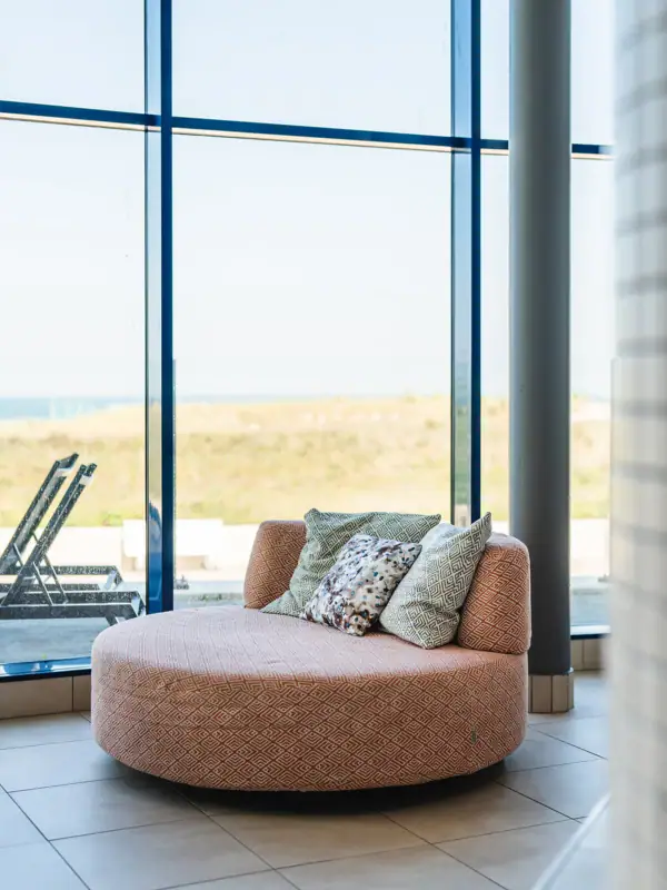 Liege  im aja Warnemünde Runde Couch mit Kissen vor einem Fenster.