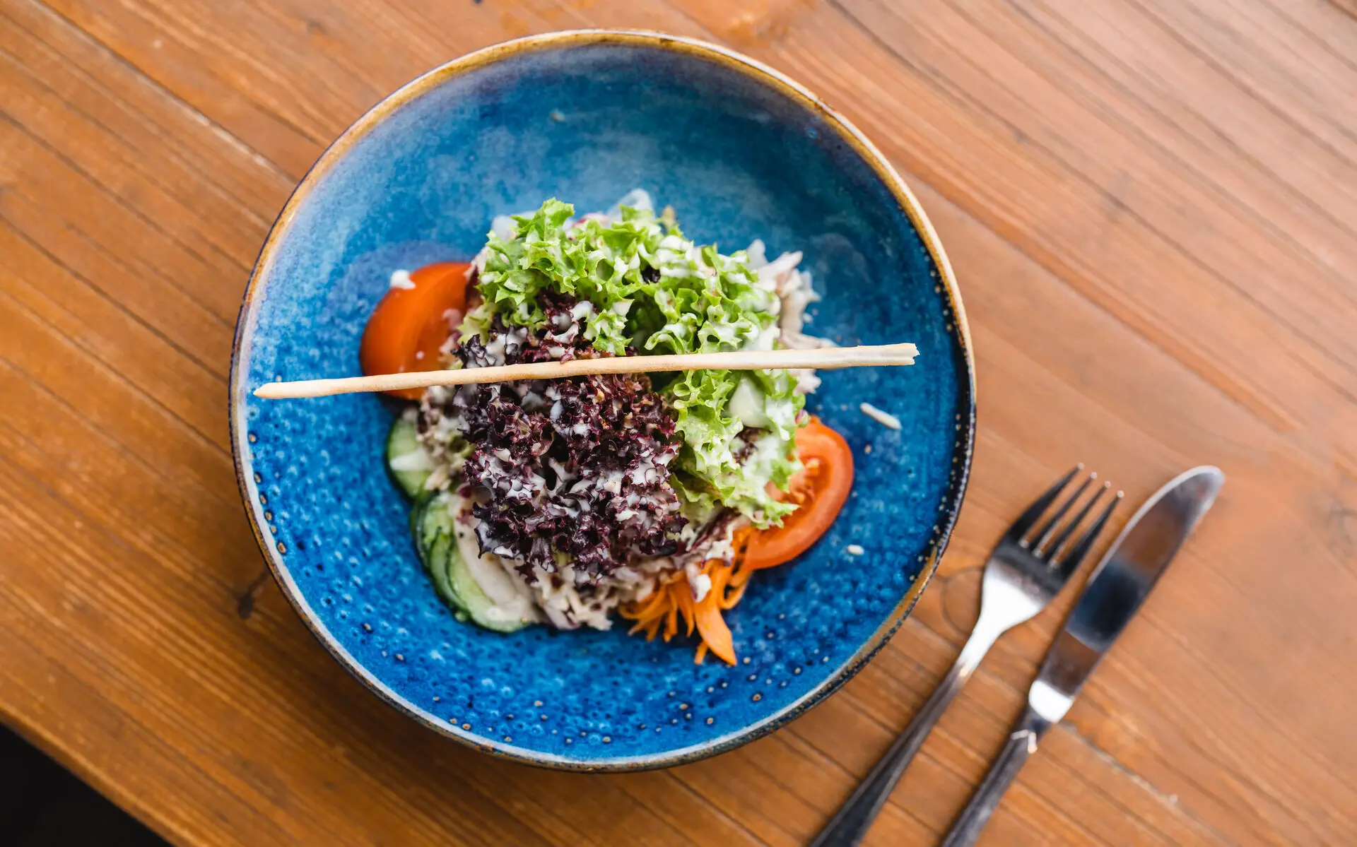 vegetarisches Gericht Auf einem Holztisch steht eine blaue Schüssel mit Salat.