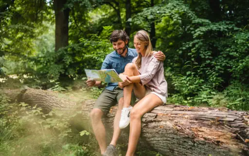 Ein Mann und eine Frau sitzen auf einem Baumstamm und betrachten eine Karte. Ein Mann und eine Frau sitzen auf einem Baumstamm und betrachten eine Karte.