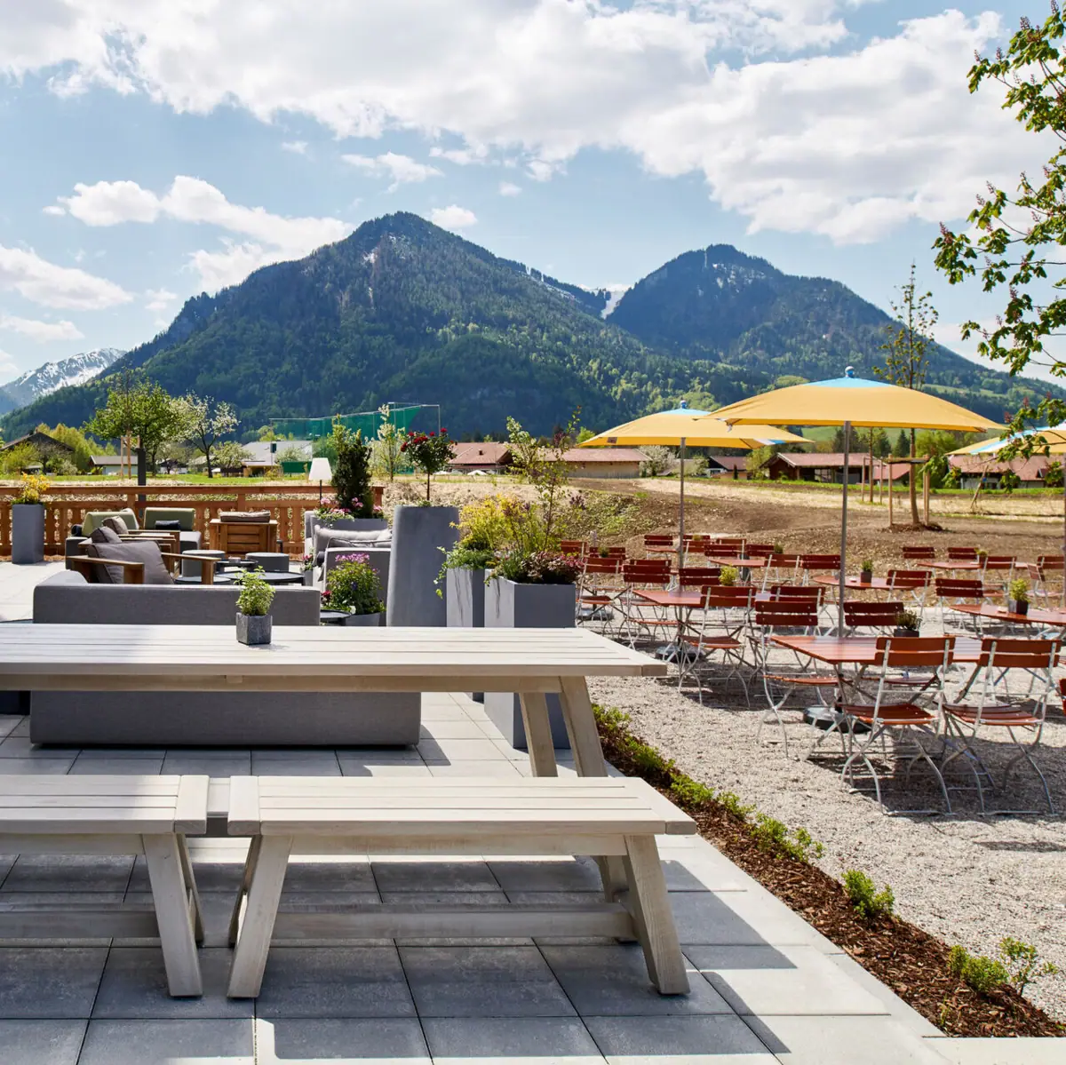 Biergarten Eine Terrasse mit Tischen und Stühlen vor einem Berg im Hintergrund.