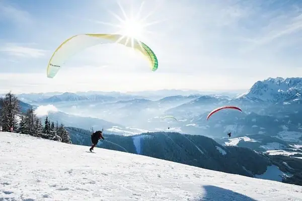 Gruppe von Personen beim Paragliden auf einem verschneiten Berg.