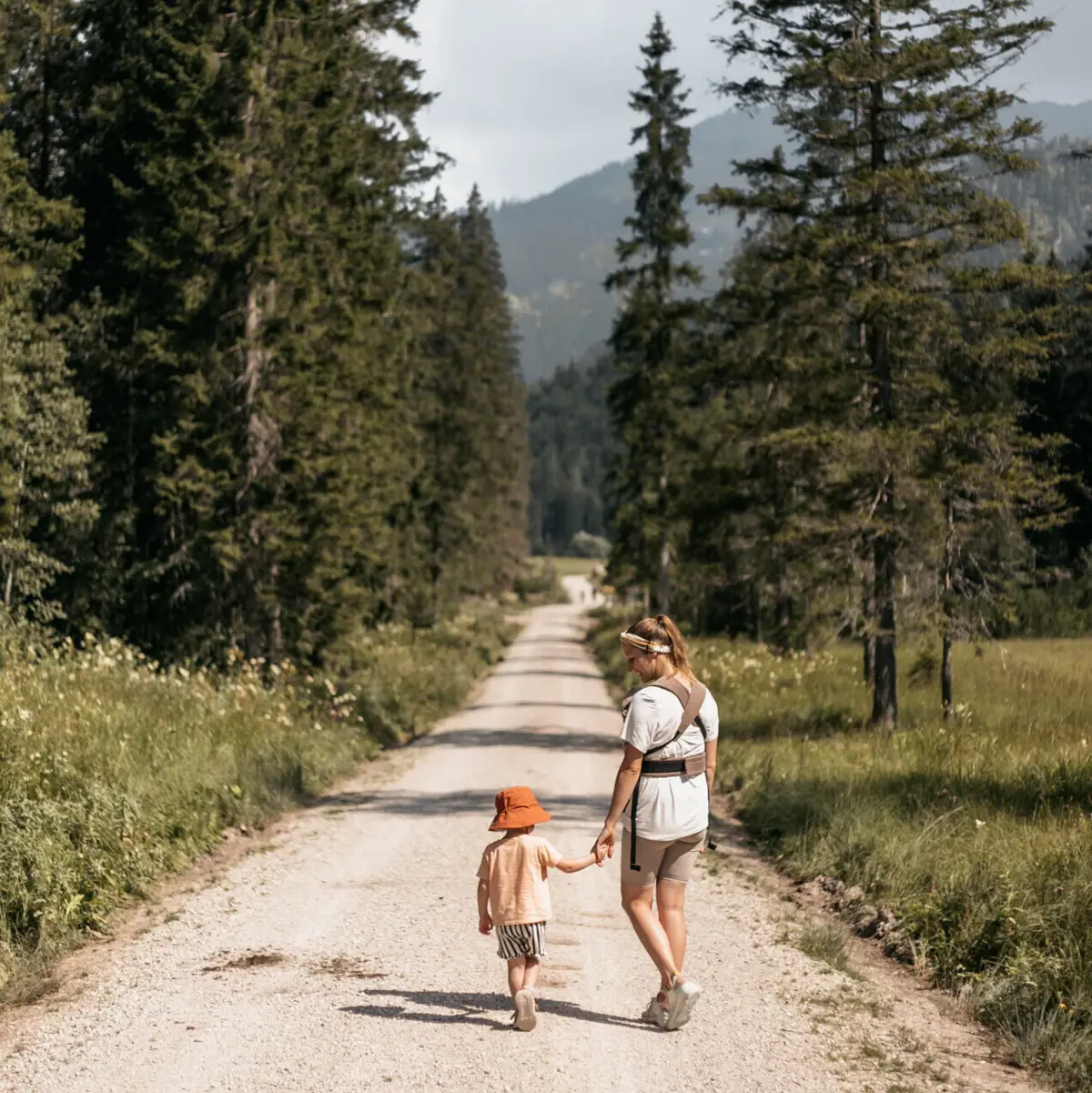Wandern mit Kindern Eine Frau und ein Kind gehen auf einem Feldweg mit Bäumen.