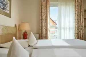 Doppelzimmer landseitig Ein Bett mit weißen Laken und einer Lampe in einem Raum mit Fenster.