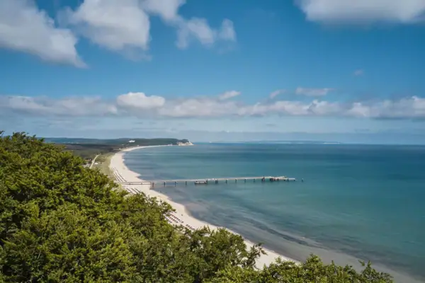 Küste von Rügen Strand mit einem Pier und Bäumen, umgeben von Wasser und Himmel.