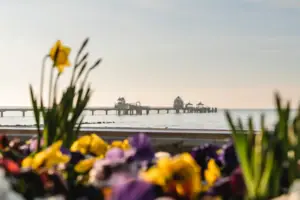 Frühling in Grömitz Ein Pier mit einer Brücke in der Ferne, umgeben von Wasser und Himmel.