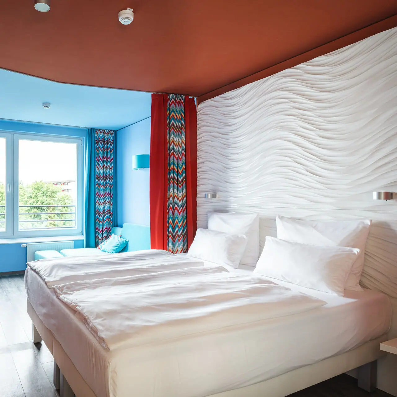 aja Grömitz Zimmer Ein Hotelzimmer mit einem großen Betten und roten Vorhängen.