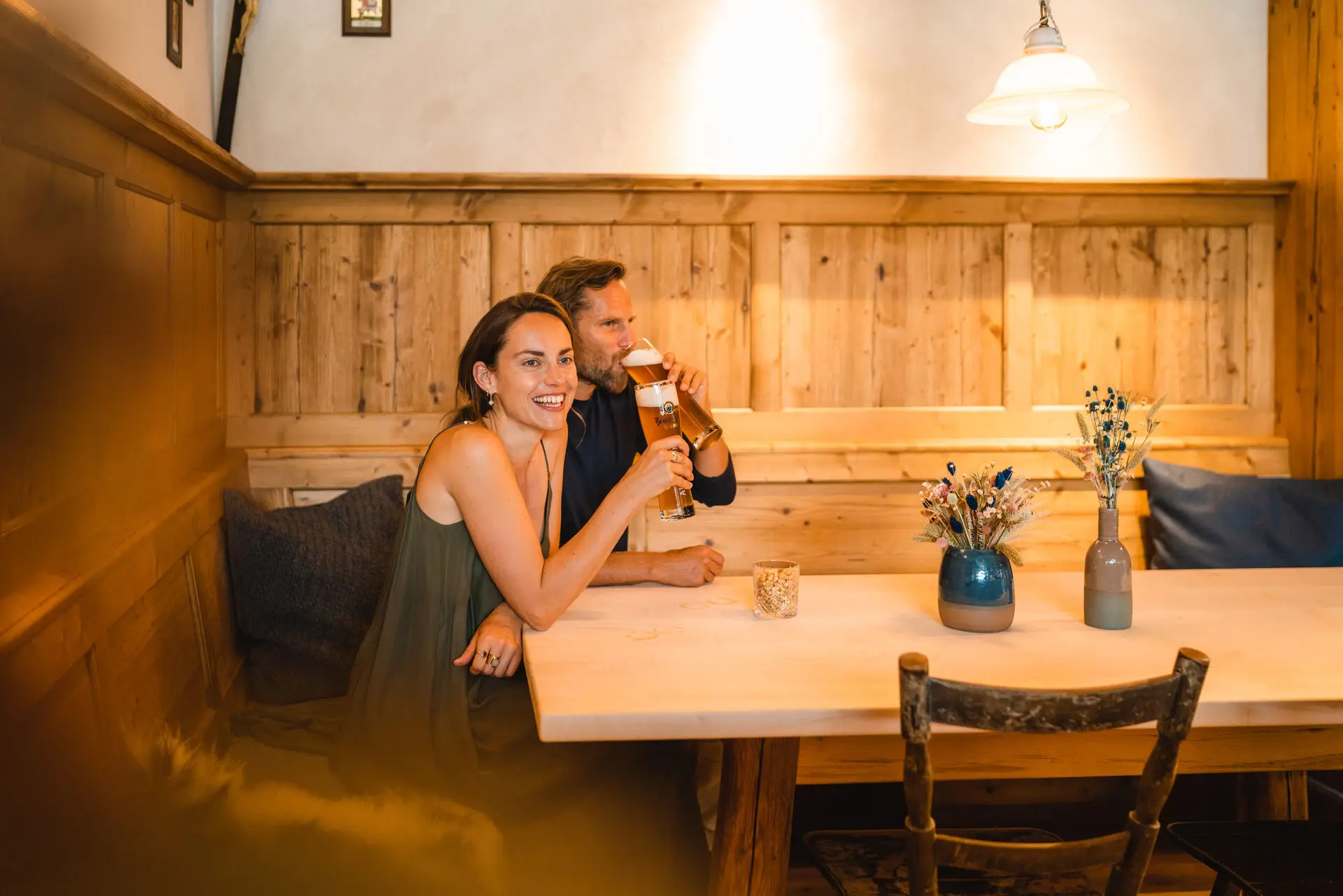 Ein Paar sitzt in einem Restaurant an einem Ecktisch mit Holzverkleidung und trinkt Bier.