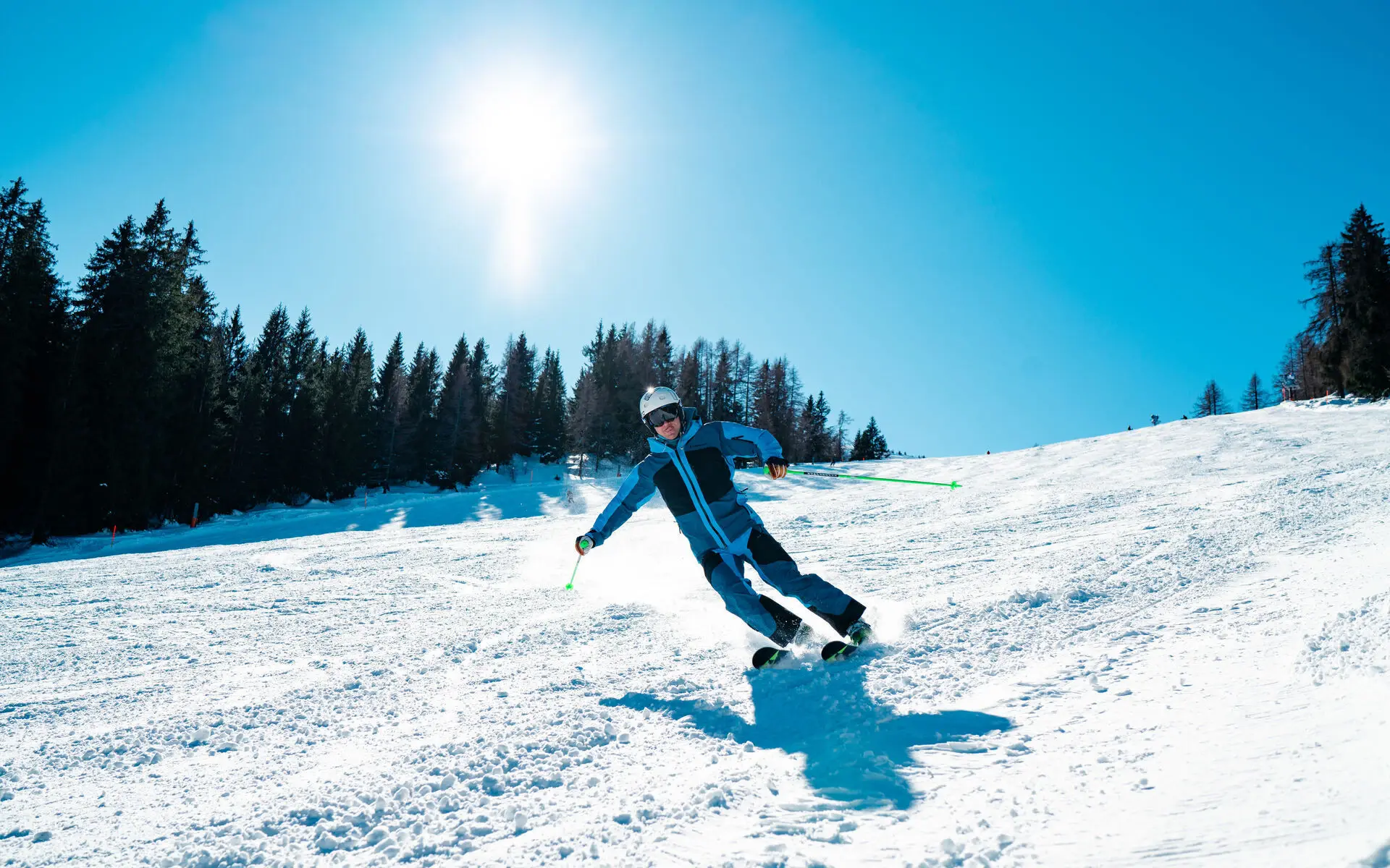 Eine Person in blauer Skiekleidung fährt einen schneebedeckten Hang bei klarem Himmel und Sonnenschein herunter.