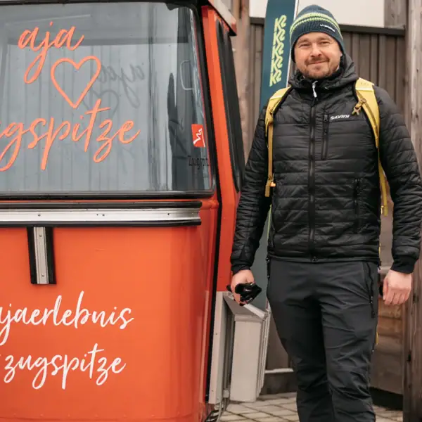 aja Gondel Ein Mann steht neben einem kleinen orangefarbenen Container.