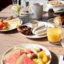Frühstück Ein gedeckter Frühstückstisch mit Früchten, Aufschnitt und Getränken auf einer Terrasse in der Sonne.