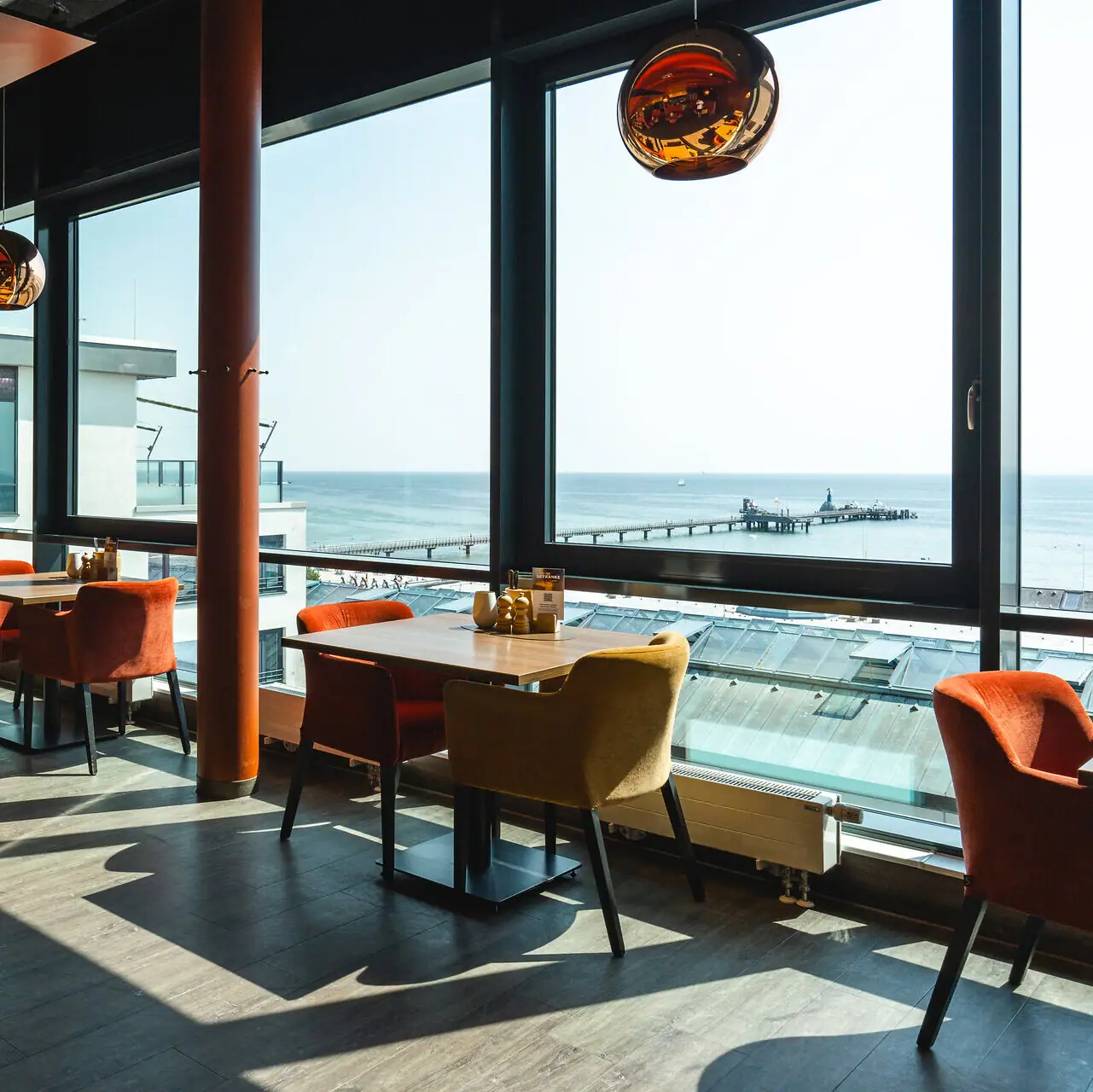 aja Restaurant Grömitz Das aja Restaurant in Grömitz mit Tischen und Stühlen und einem Fenster mit Blick auf die Ostsee und die Seebrücke.