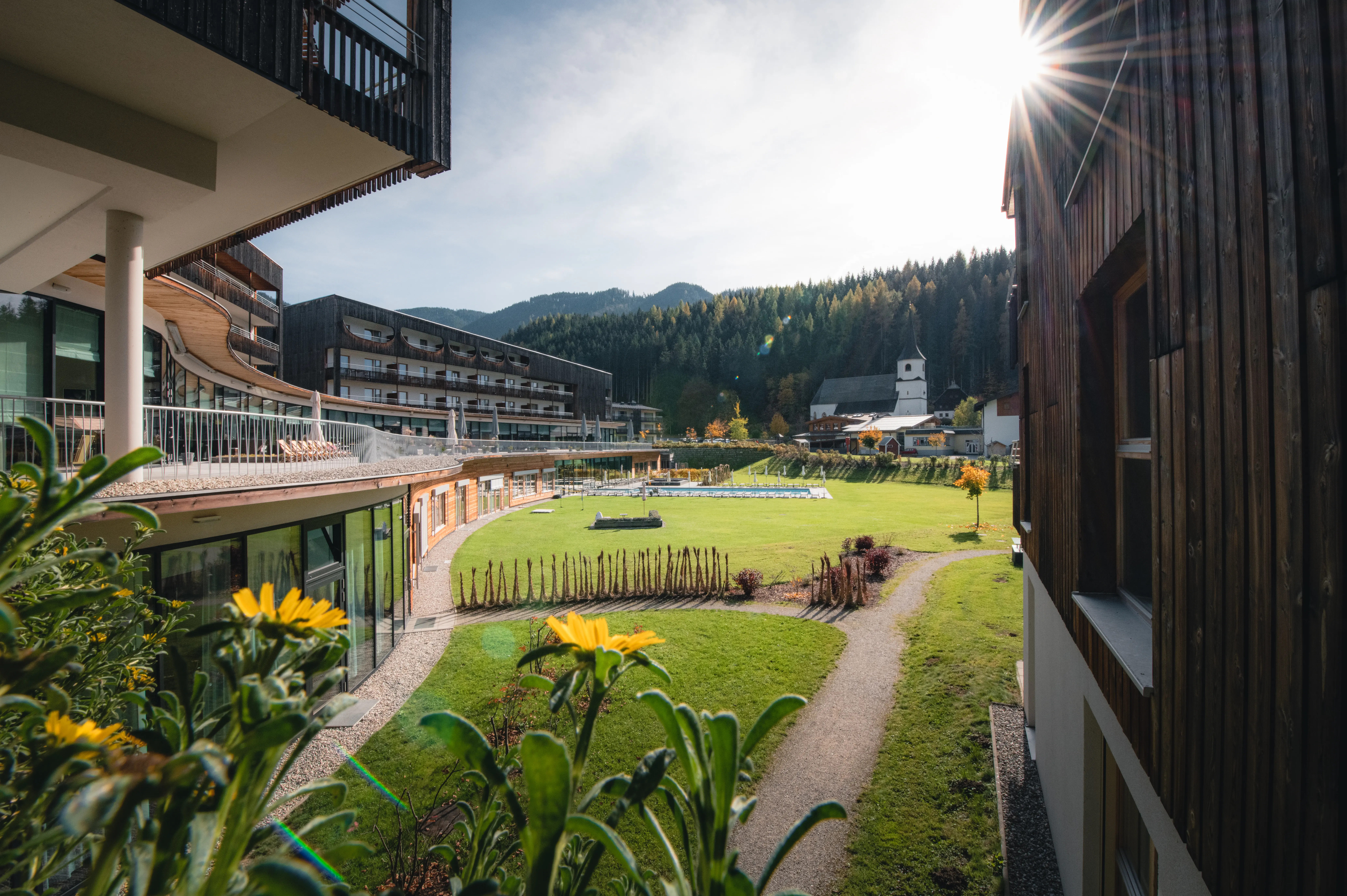 aja Bergresort Werfenweng Grüne Wiese mit Bäumen und Gebäuden im Hintergrund.