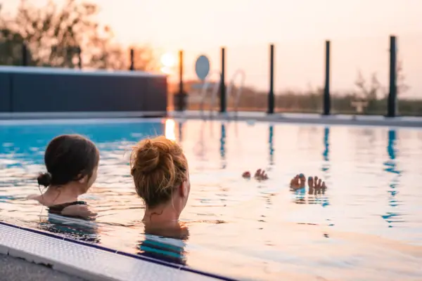 Außenpool Zwei Frauen schwimmen in einem Außenpool bei Sonnenuntergang.