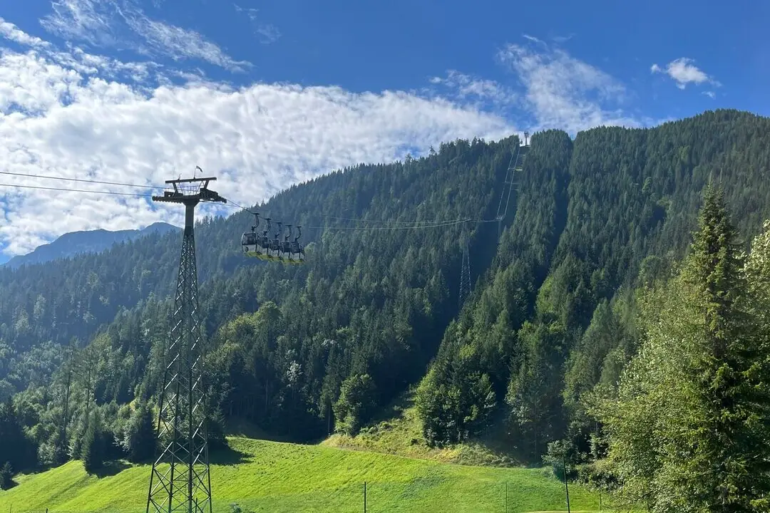 Karwendel Bergbahn Stromleitung in einem grasbewachsenen Feld mit Bäumen und blauem Himmel