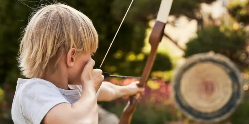 Ein blonder Junge spannt einen Bogen und zielt auf eine Scheibe. Ein blonder Junge spannt einen Bogen und zielt auf eine Scheibe.