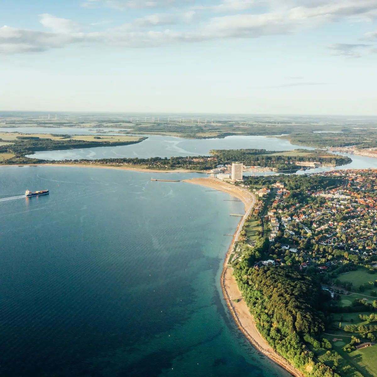 Travemünde von oben Luftaufnahme einer Küstenstadt mit Blick auf eine große Wasserfläche und bewölktem Himmel.