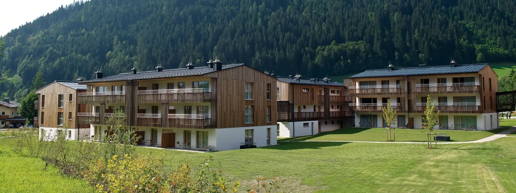 aja Ferienwohnungen Werfenweng Ein Pool im Freien vor Gebäuden mit Bäumen und klarem Himmel.
