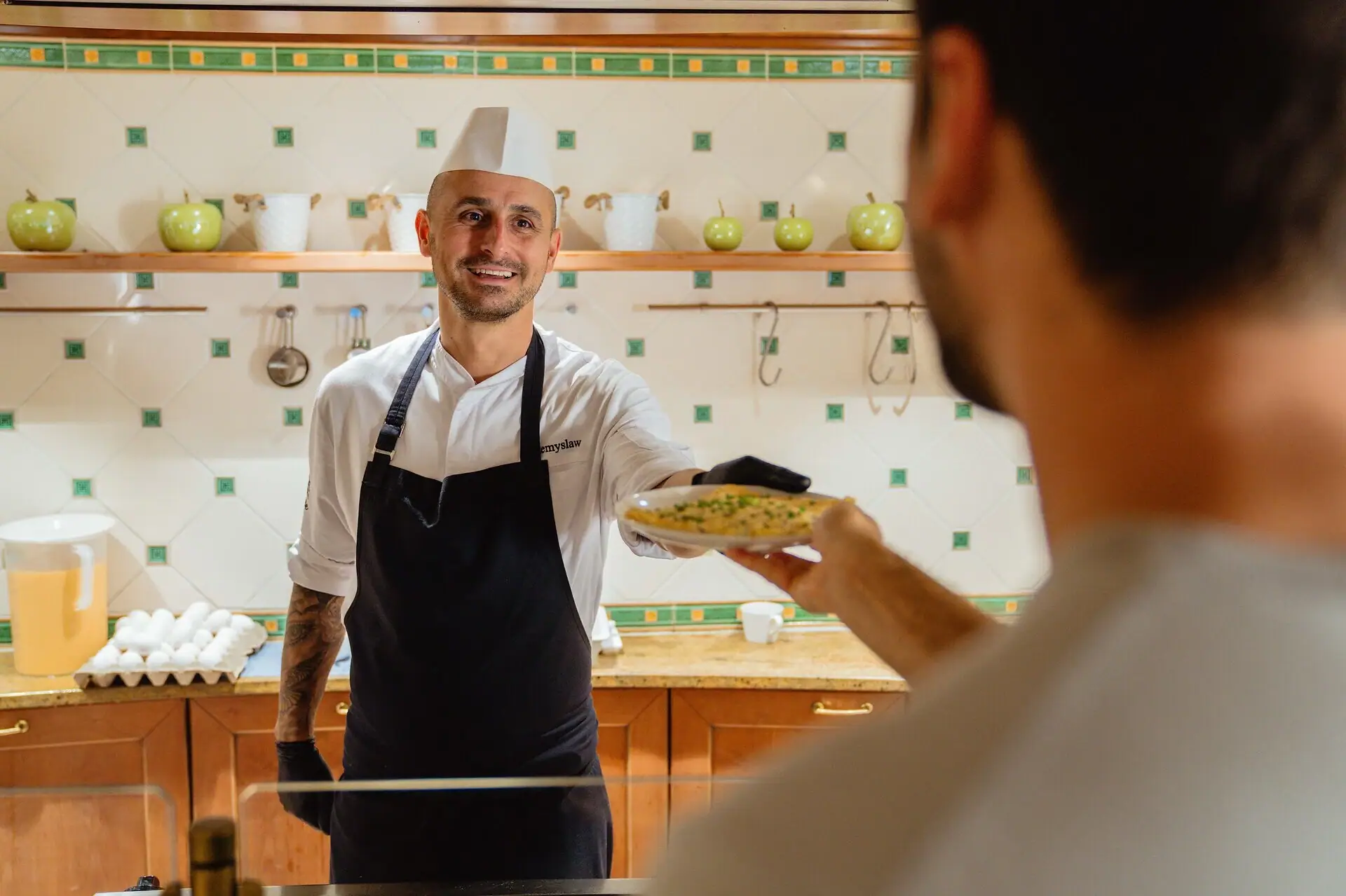 Omlett Ein Mann mit Kochmütze reicht einem anderen Mann einen Teller mit Essen.