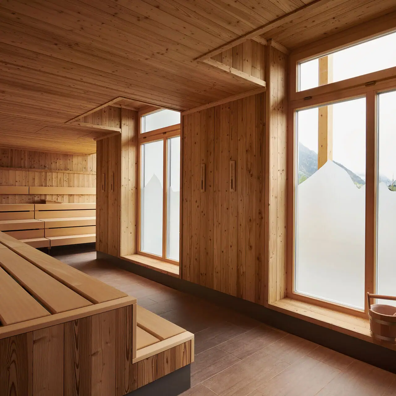 Sauna im aja Ruhpolding Ein Raum mit einer Holzbank und Fenstern.
