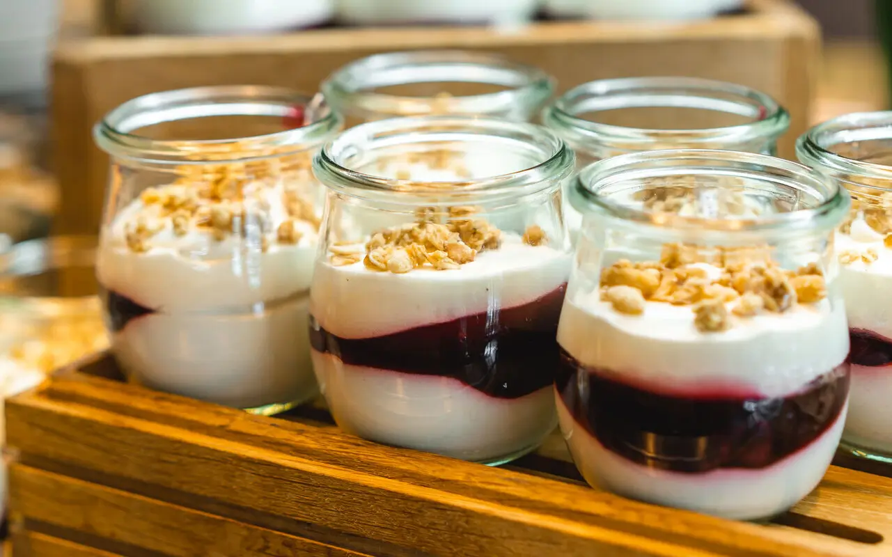 Dessert im aja Travemünde Kleine Gläschen mit Quarkspeise und einer einer dazwischen geschichteten roten Sauce stehen auf einem Holztablett.