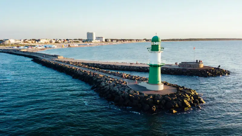 Grüner und weißer Leuchtturm auf Felsen im Wasser.