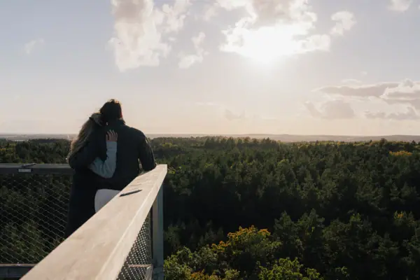 Baumwipfelpfad Usedom Ein Mann und eine Frau umarmen sich auf einem Balkon mit Blick auf dem Baumwipfelpfad Usedom.